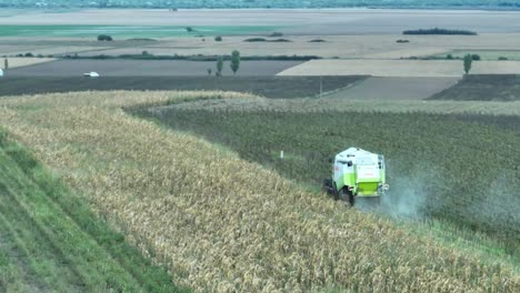 Aerial-view-of-German-Claas-Harvester-cutting-plants-on-field-in-rural-area-with-traffic-on-road-in-background
