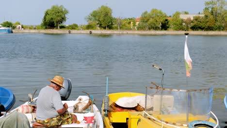 Man-sits-on-boat-reparing-his-fishing-net-in-sozopol-marina-dock