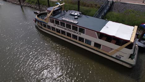 Floating-pancake-restaurant-all-you-can-eat-Pannenkoekenboot-at-anchor-seen-from-above-on-the-shore-of-historic-Hanseatic-city-of-Nijmegen-in-waiting-for-passengers-in-river-Maas