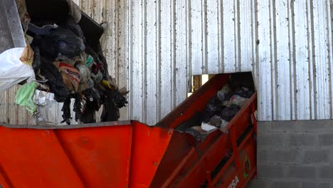 A-bulldozer's-bucket-dumps-the-waste-into-a-conveyor-belt's-hopper-inside-a-waste-processing-plant