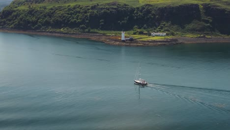 Aerial-drone-shot-of-a-boat-sailing-past-the-Tobermory-Lighthouse-and-the-Isle-of-Mull-coastline