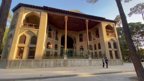 Wide-view-of-Persian-palace-Hasht-Behesht-pavilion-with-wooden-column-brick-architecture-design-people-walking-cyclist-riding-pine-trees-in-Cultural-capital-of-Empire-Esfahan-in-sunset-time-Isfahan