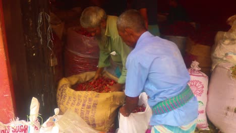 Two-Asian-men-filling-sacks-by-hand-with-red-chili-at-the-market