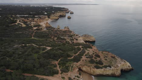 Benagil-caves-aerial-view-over-rock-formation-woodland-coastline,-Algarve-Portugal-scenic-Atlantic-ocean-skyline