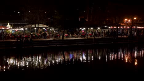 Scenic-Night-Bar-by-the-Lake:-People-Enjoying-Drinks-with-Reflections-of-Lights-on-Water