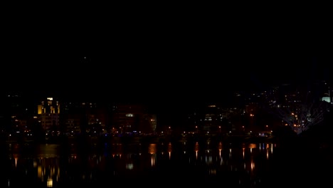 Laser-spotlights-enlightening-the-sky-over-city-at-night-near-reflecting-water-surface-in-Tirana