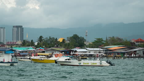 Old-Wooden-Houses-And-Various-Travel-Tour-Boats-on-Water-in-Bay-Area-of-Kampung-Tanjung-Aru-Lama-District,-Low-Income-People's-Homes-In-Sabah,-Kota-Kinabalu