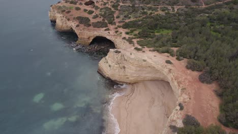 Aerial-view-descending-over-Benagil-caves,-Lagoa,-Algarve-Portugal-with-Atlantic-ocean-transparent-coastline