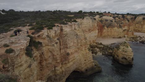 Aerial-view-passing-tourists-sightseeing-on-Benagil-caves-cliffs-overlooking-scenic-Atlantic-ocean-Algarve-coastline
