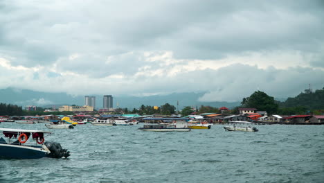 Schwimmende-Reiseboote-Und-Häuser-Auf-Dem-Wasser-In-Der-Bucht-Von-Kampung-Tanjung-Aru-Lama-District,-Kinabalu-Berg-Im-Hintergrund-In-Sabah,-Kota-Kinabalu