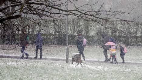 People-walking-children-to-school-in-blizzard-snow-cold-weather-in-windy-UK-winter-storm-conditions