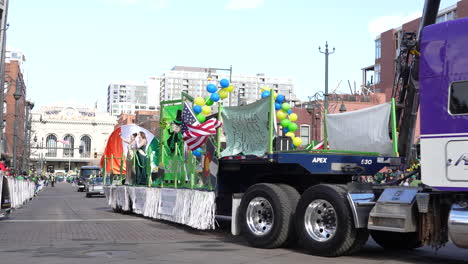 Purple-semi-truck-pulling-a-parade-float-with-people-waving-to-the-crowd-in-a-Saint-Patrick's-Day-parade