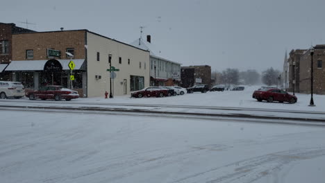 Small-town-street-with-cars-and-snow-falling-in-winter-day