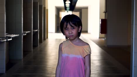 Portrait-of-a-young-Southeast-Asian-boy-alone-scared-looking-into-camera-in-an-abandoned-mall-hallway-with-light-and-shadow-in-the-background