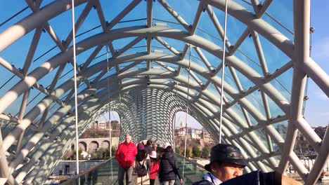 Walking-on-the-Bridge-of-Peace-in-Tbilisi,-Georgia-with-crowded-people-and-tourists-in-the-morning-on-December-26,-2018-during-winter