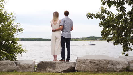 Attractive-young-couple-staring-out-across-a-beautiful-lake-as-a-boat-drives-by