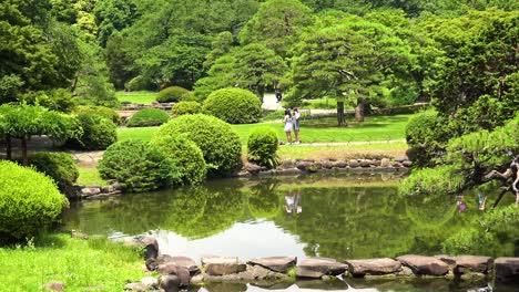 Verkleinern-Sie-Den-Blick-Auf-Den-See-Mit-Menschen-Und-Baumspiegelungen-Im-Shinjuku-Gyoen-Nationalgarten