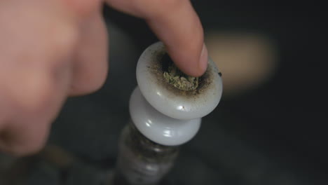 Marijuana-is-pushed-into-a-white-bong-bowl-by-a-finger