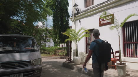 Tourist-with-a-backpack-walking-in-the-street-with-bars-and-hotels-of-Zanzibar-Stone-Town