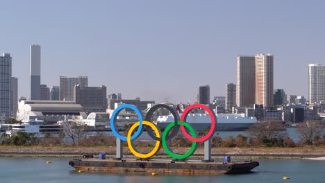 Olympic-Games-sign-in-Tokyo-Bay-with-ships-passing-in-background-on-bright-and-sunny-day