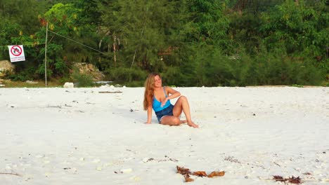 Happy-attractive-Caucasian-woman-smiling-on-white-sandy-beach-relaxing-in-front-of-sunlight,-green-tropical-plants-background