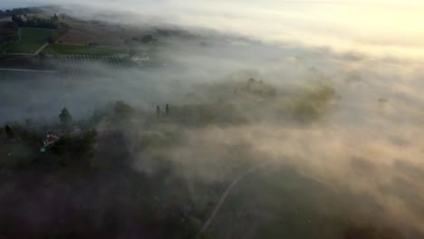 Tuscany-hills-covered-in-morning-mist-clouds-at-sunrise,-aerial-drone-view