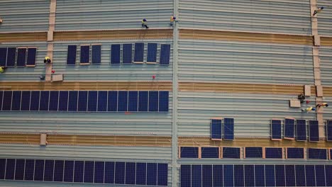 Aerial-top-down-view-of-many-industrial-workers-installing-solar-panels-on-roof-for-renewable-energy