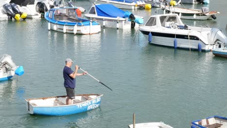 A-man-casually-rows-stood-up-in-a-small-boat-in-a-busy-harbour