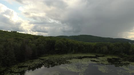 Cloudy-stormy-day-viewed-by-drone-taking-off-and-rising-over-lake-and-mountain