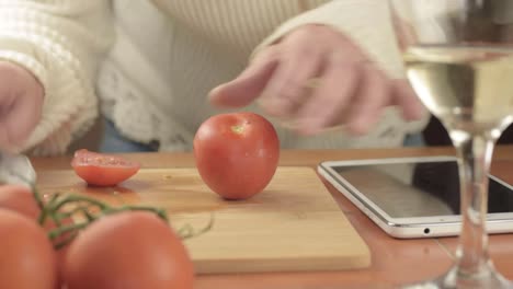 Manos-Cortando-Tomates-De-Vid-Frescos-En-La-Cocina-Con-Receta-En-Tableta-De-Tiro-Medio