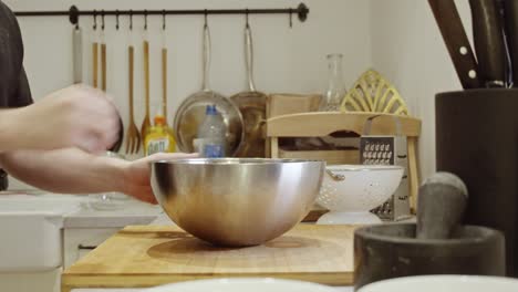 Chef-puts-out-metal-bowl-on-the-wooden-cooking-table