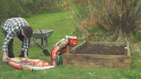 Young-man-places-bags-of-compost-against-raised-bed-on-garden