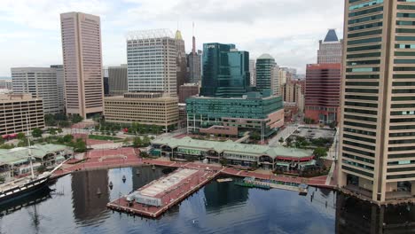 Rising-aerial-tilt-reveals-shopping-and-clipper-ship-in-Marina-at-Baltimore-Inner-Harbor,-urban-city-skyline