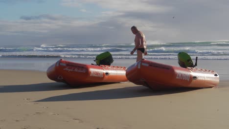 Man-Walking-On-The-Beach-Towards-The-Ocean---Two-Inflatable-Rubber-Boat-In-Currumbin-Beach---Gold-Coast,-Queensland,-Australia