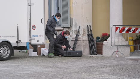 A-Couple-of-Guys-Working-Outside-a-Building,-in-Town,-While-Wearing-a-Medical-Mask