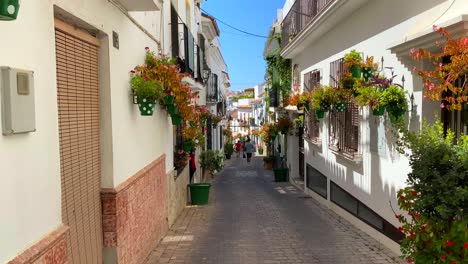 Walking-in-a-typical-narrow-Spanish-street-in-old-city-Estepona-with-houses,-colorful-flower-pots-and-beautiful-balconies
