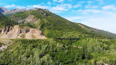 4K-Drone-Video-of-Train-Trestle-bridge-and-Mountains-Rising-above-the-Chulitna-River-near-Denali-National-Park-and-Preserve,-AK-during-Summer