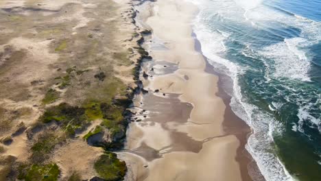 Flying-over-a-beach,-across-dunes-and-waves