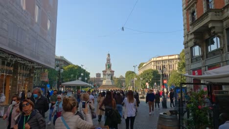 Via-Dante-überfüllte-Straße-Mit-Menschen,-Die-Spazieren-Gehen-Und-Einkaufen,-Und-Castello-Sforzesco-Im-Hintergrund,-Italien