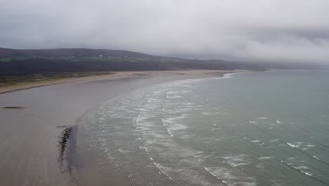 AERIAL:-High-flight-across-overcast-Beach-with-crashing-waves,-Oxwich,-4K-Drone