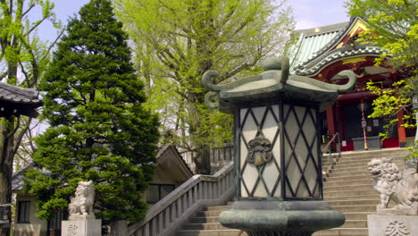ASAKUSA,-TOKYO,-JAPAN-circa-April-2020:-a-woman-worshipping-at-authentic-Japanese-temple,-with-tree-lines-and-stairs,-traditional-lanterns-in-peaceful-and-quiet-zen-style-garden-on-sunny-day