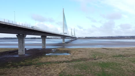 Mersey-gateway-landmark-toll-bridge-at-low-tide-with-river-marshland-aerial-view-rising-low-to-high-forwards-shot