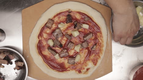 Colocando-Queso-En-Cubos-Sobre-Masa-De-Pizza-Cubierto-Con-Carne-Y-Salsa-De-Pizza-Antes-De-Hornear