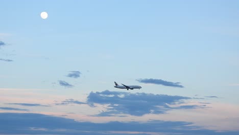 Distant-passenger-airplane-plane-flies-under-moon-in-cloudy-sky