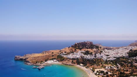 Luftaufnahme-Des-Strandes-Von-Lindos,-Der-Weißen-Häuser-Des-Dorfes-Und-Der-Akropolis-Im-Hintergrund,-Rhodos,-Griechenland---Drohnenaufnahme