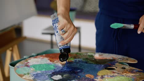 Unrecognizable-woman-pouring-blue-paint-on-a-painting-palette