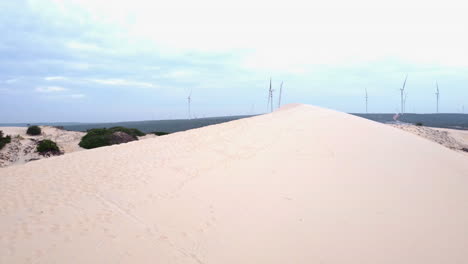Weiße-Sanddüne-Mit-Windenergiepark-Am-Horizont,-Bewegungsansicht