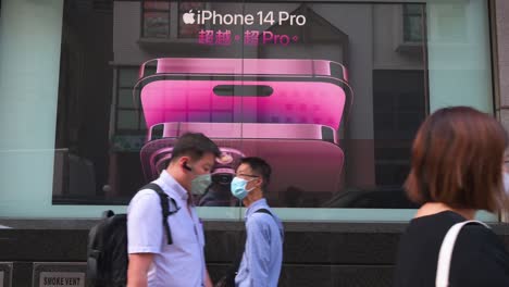 Pedestrians-wearing-face-masks-walk-past-a-commercial-advertisement-from-the-American-multinational-technology-company-Apple-showcasing-the-iPhone-14-Pro-smartphone-in-Hong-Kong