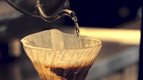Pouring-hot-water-in-a-drip-coffee-filter-full-of-coffee-grounds-in-slow-motion