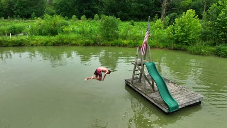 Young-teenage-boy-doing-a-back-flip-off-of-floating-island-in-pond